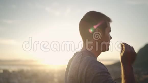 日出时一名男跑运动员站在山顶顶天立地在跑步前将耳机插入耳朵运动员视频的预览图