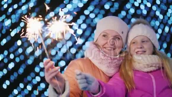 妈妈和女儿在模糊的圣诞树灯光的背景下玩火花视频的预览图