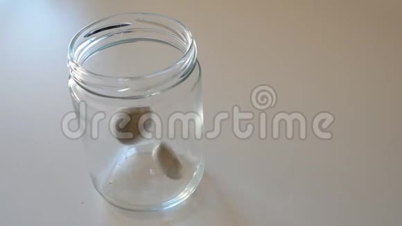 两个欧元硬币掉进一个白色背景的玻璃罐子里视频的预览图