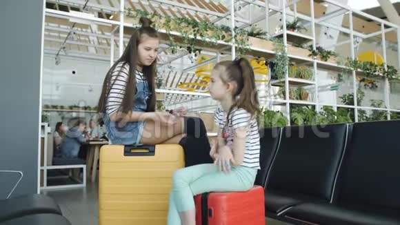 姐妹们坐在机场休息室的一个鲜艳的彩色手提箱上聊天视频的预览图