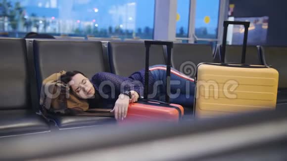 一个女人睡在机场候机楼的长凳上在飞机上等待长时间的转机视频的预览图