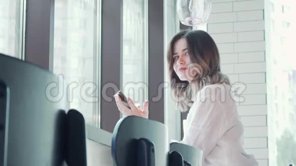 可爱的女人在咖啡店用智能手机向美洲微笑视频的预览图