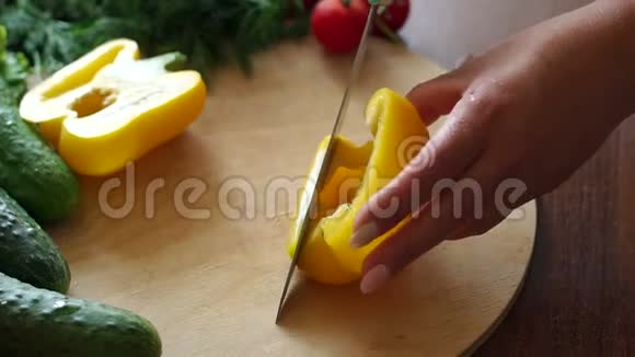 一名妇女在木制砧板上切鲜黄色甜椒的特写镜头视频的预览图
