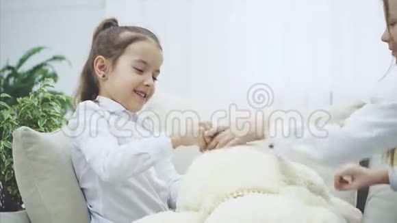 两个可爱的快乐女孩在玩泰迪熊调整它的蝴蝶结拥抱他们的毛绒朋友视频的预览图