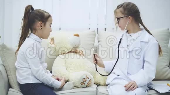 两个可爱的孩子在玩泰迪熊扮演医生的女孩正在用听诊器检查长毛绒熊说话视频的预览图