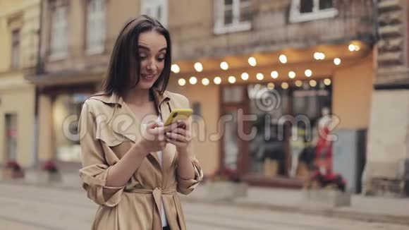 年轻迷人的女孩看着惊讶地拿着手机聊天和笑说哇站在城市背景视频的预览图
