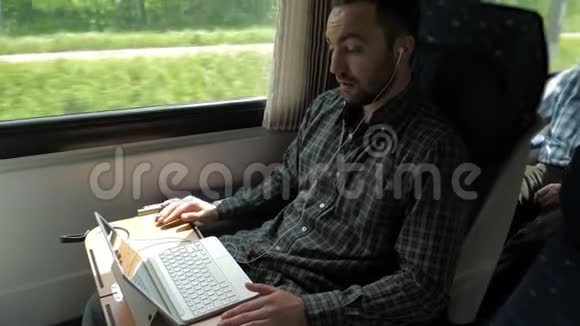 年轻的专家带着耳机在火车上用笔记本电脑通过视频聊天与雇主交谈视频的预览图