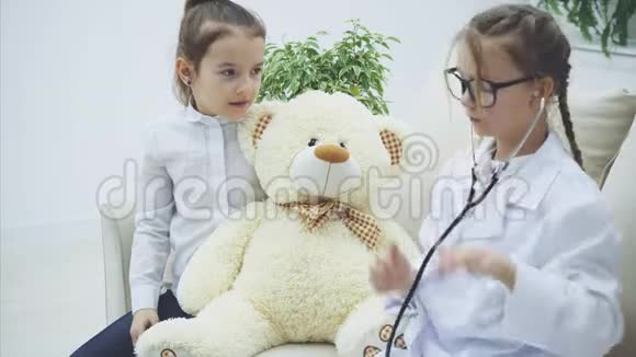 两个可爱的孩子在玩泰迪熊扮演医生的女孩正在用听诊器检查长毛绒熊说话视频的预览图