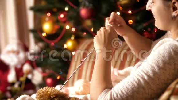 特写4k镜头年轻女子坐在扶手椅旁旁边是发光的圣诞树和为她编织羊毛衫视频的预览图