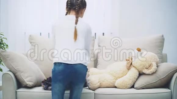 小女孩编着辫子把白色泰迪放在沙发上用毯子盖着走开了视频的预览图