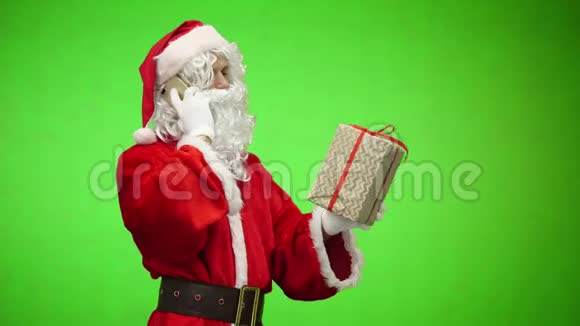 满意的圣诞老人在电话里说着笑着拿着礼物坐在桌子旁背景是绿色的视频的预览图
