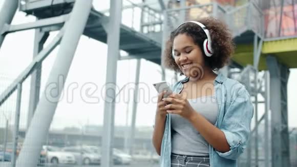 非洲裔美国妇女在外面使用智能手机享受耳机音乐视频的预览图