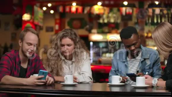 两个男人和两个女人多种族的夫妻坐在咖啡馆里看着智能手机的屏幕讨论视频的预览图