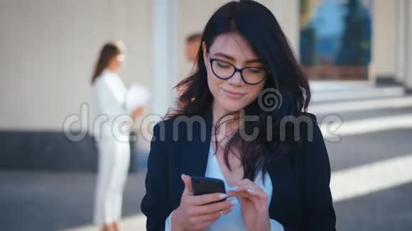 一位年轻漂亮的商务女性她带着智能手机发短信一边在外面工作一边微笑视频的预览图