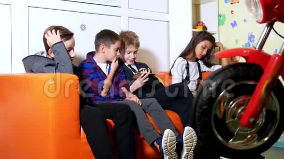 三个男孩和一个女孩坐在沙发上用手机玩电子游戏视频的预览图
