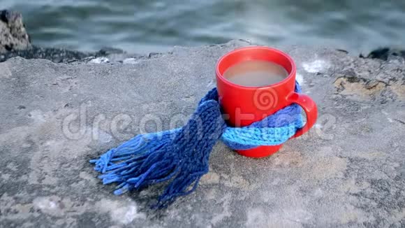 带咖啡和蒸汽的红色杯子和蓝色针织围巾站在石头上视频的预览图
