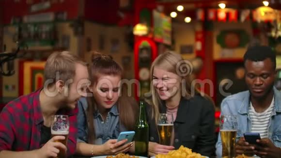 一个男人和两个女孩在朋友的陪伴下坐在酒吧里看手机屏幕视频的预览图