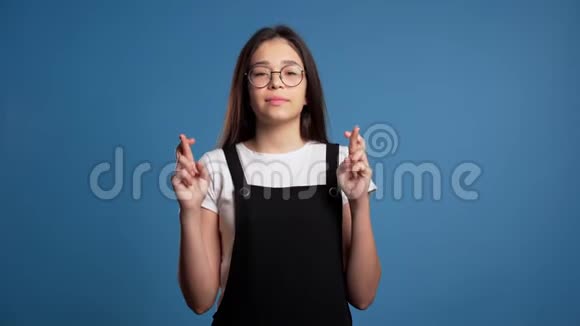 可爱的亚洲女孩在蓝色背景下祈祷戴眼镜的女人求人4k视频的预览图