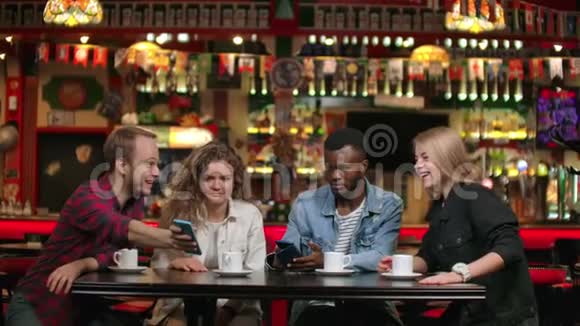 四个朋友看着手机上的照片坐在咖啡店里笑着讨论他们在咖啡店里看到的东西视频的预览图