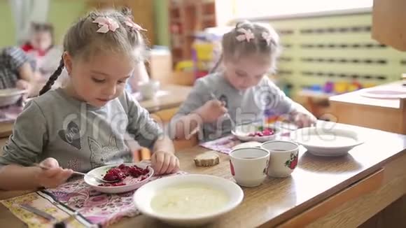 双胞胎女孩坐在幼儿园的桌子旁吃沙拉在学前班吃饭羡慕视频的预览图