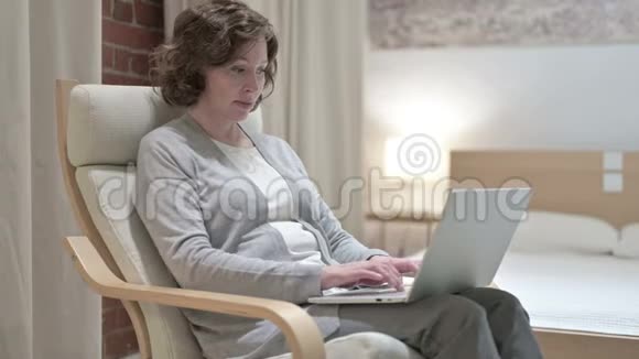悲伤的老女人面对沙发上的笔记本电脑视频的预览图