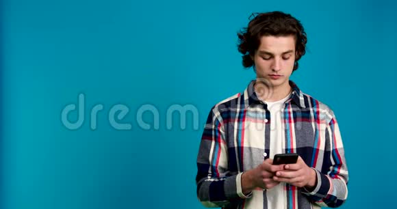 年轻男子使用智能手机目光移开摇头与蓝色背景隔绝视频的预览图