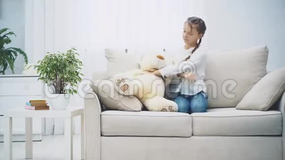 小女孩坐在沙发上看着心烦意乱和无聊然后拥抱一个大泰迪熊微笑永远的朋友视频的预览图
