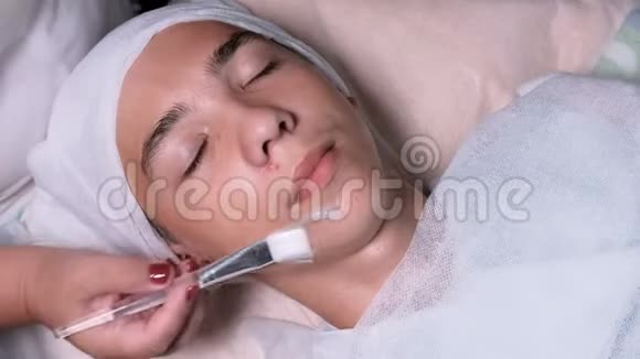 在一个十几岁的男孩的脸上涂胶刷的美容师的手的特写男性客户面部美容视频的预览图