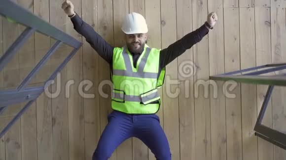 微笑的建筑工人在头盔和绿色夹克躺在地板上显示胜利的手势和抬头职业视频的预览图