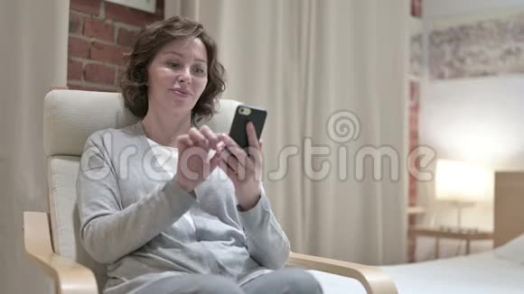 卧室里使用智能手机的老女人视频的预览图