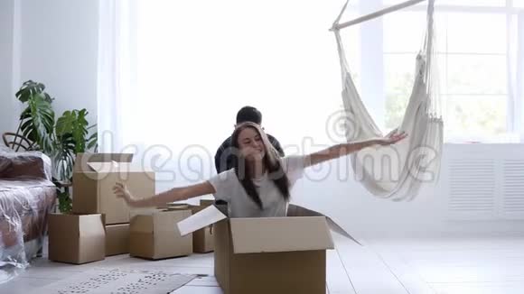 幸福的已婚夫妇在新房子里一起玩得很开心休息一下打开行李女孩骑着一个纸箱她丈夫视频的预览图