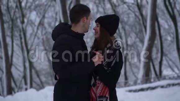 美丽的年轻女人和男人交谈互相看着对方眼睛在冬天的公园下降雪人类温暖了双手视频的预览图