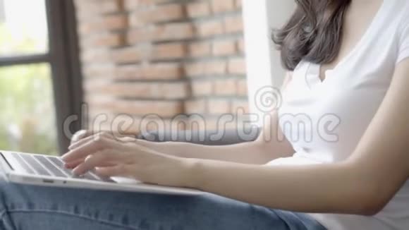 在客厅的沙发上展示笔记本电脑的年轻亚裔女性自由职业和社交网络视频的预览图