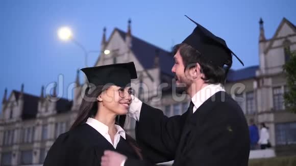 两个快乐的应届毕业生男研究生帮女生校正帽子她对他微笑视频的预览图
