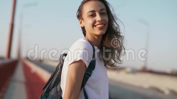 年轻的成年女性模特在户外摆姿势穿着白色t恤的快乐轻松的漂亮女人站在蓝色的桥上视频的预览图