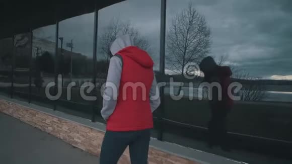 阴天穿红色无袖夹克的女孩走在大窗户旁边视频的预览图