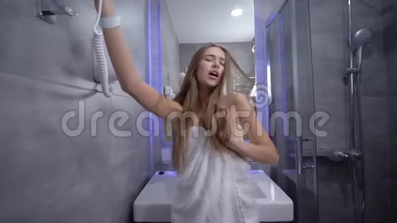 淋浴间充满乐趣美丽性感的年轻女子穿着毛巾唱歌手里拿着吹风机前边调情视频的预览图