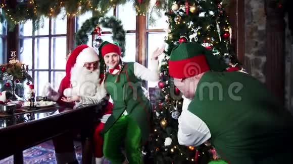 精灵和圣诞老人在圣诞树附近拍照精灵正在装饰的房间里拍摄一个快乐的仙女角色视频的预览图