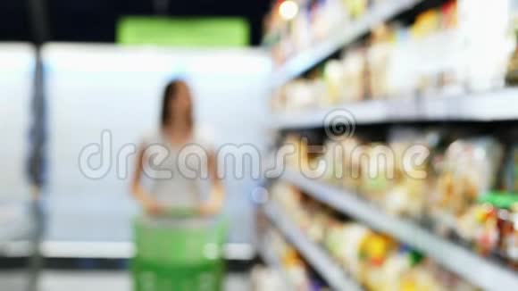 女人带着绿色的购物车在商店里模糊地走到镜头前在货架之间挑选商品视频的预览图
