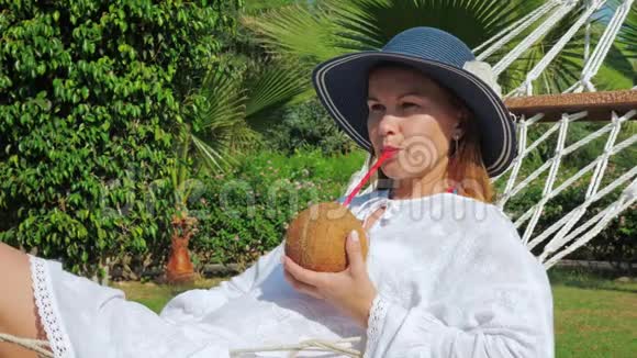 年轻女子躺在吊床上用椰子水鸡尾酒视频的预览图