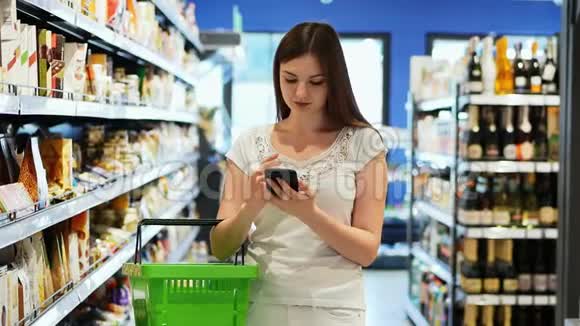 漂亮的女人在超市里用手机和购物篮发短信视频的预览图