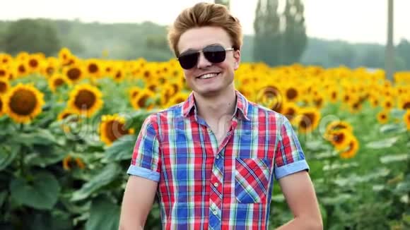 酷又时尚的年轻男农民带着太阳镜成功地站在向日葵的背景田野上视频的预览图