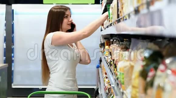 快乐的女人选择超市里的产品用手机交谈顾客选择货架上的商品视频的预览图