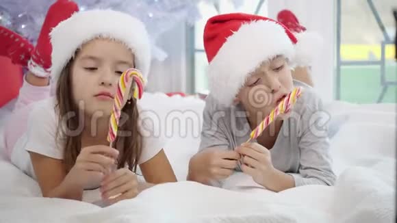 可爱的穿着睡衣的哥哥姐姐在冬天的早晨舔圣诞糖果的视频视频的预览图
