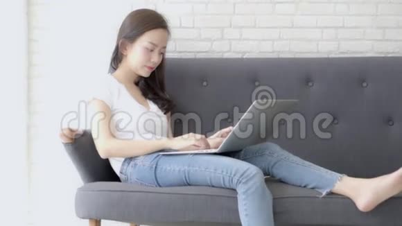 美丽的年轻自由职业亚洲女性微笑着在沙发上工作和打字视频的预览图