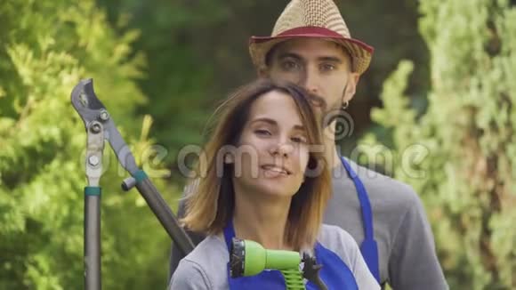 美丽的白种人女人和穿着蓝色制服的英俊男子站在花园里拿着花园工具的画像视频的预览图