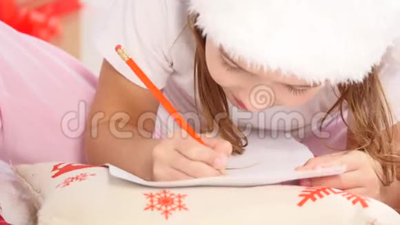在寒冷的冬天早晨戴着圣诞帽的小女孩在圣诞树附近给圣诞老人写信视频的预览图