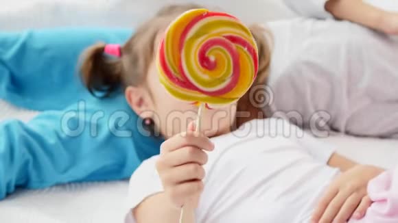 可爱的视频华丽的孩子与有趣的辫子醒来正在舔红黄色的糖果棒微笑可爱视频的预览图
