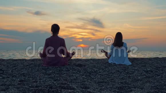 两位年轻女性在日落时在海边或海洋练习瑜伽视频的预览图