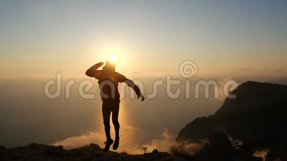 一个乐观的年轻人在空中跳跃和抓腿的剪影以缓慢的运动对抗美丽的日落视频的预览图